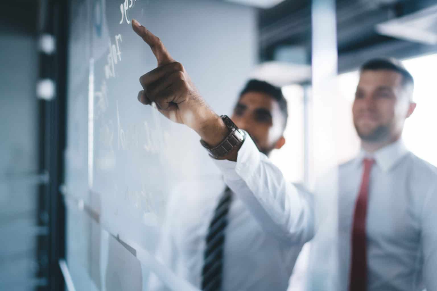 two men looking at glass board with one pointing