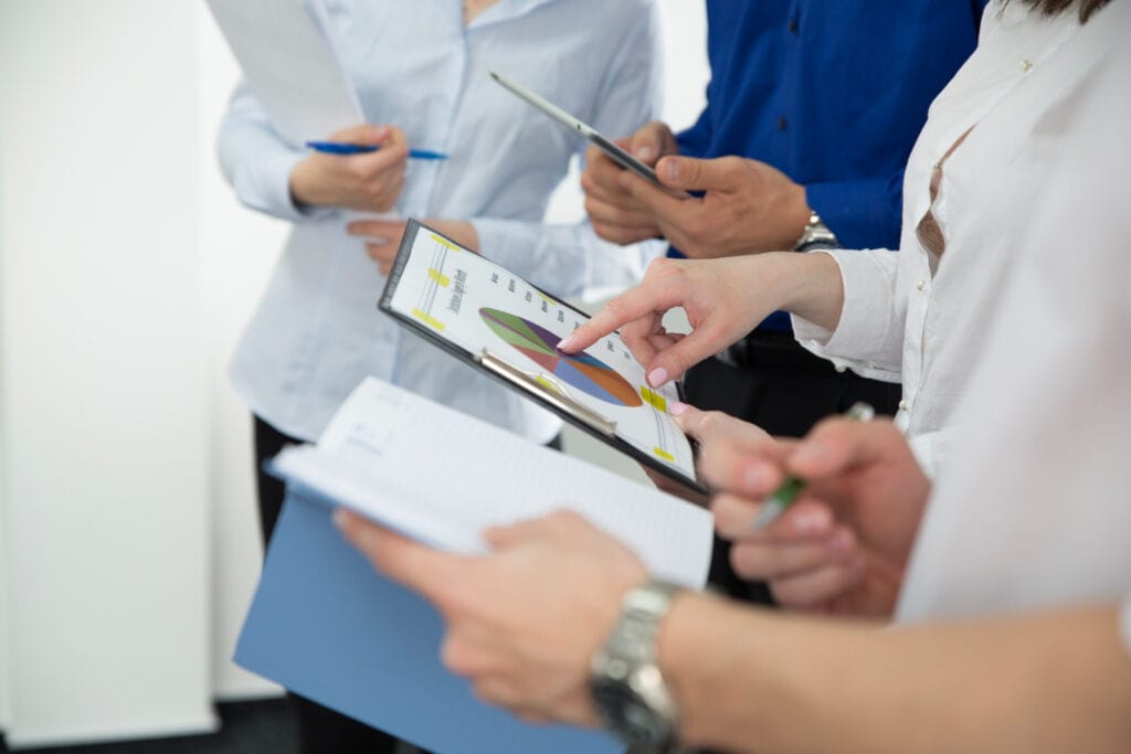 Office workers gathered with one pointing at the chart in ther hand