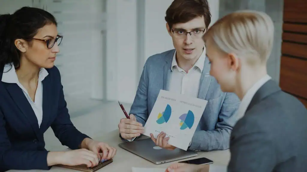 Three project controllers gathered in office, one man is holding a report and is showing it to the two women